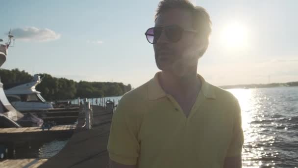 Bello bell'uomo maturo che indossa occhiali da sole, molo yacht in marina sullo sfondo. — Video Stock