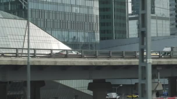 電車の窓から都市の景色。車と道路との橋の建設。背景の高層ビル. — ストック動画