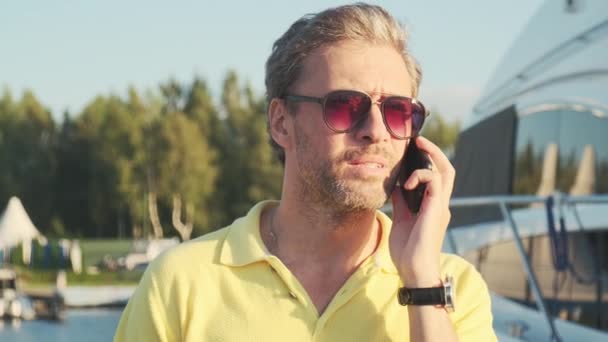 Un hombre guapo y exitoso en el yate hablando por teléfono móvil. Retrato del hombre de negocios en velero al atardecer. — Vídeos de Stock