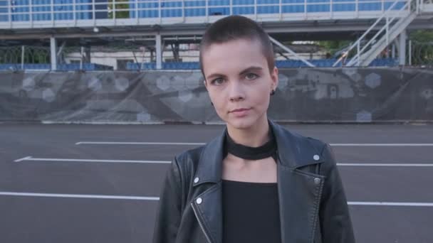 Portrait of smiling young woman with short hair in industrial city background at sunset. — Stock Video