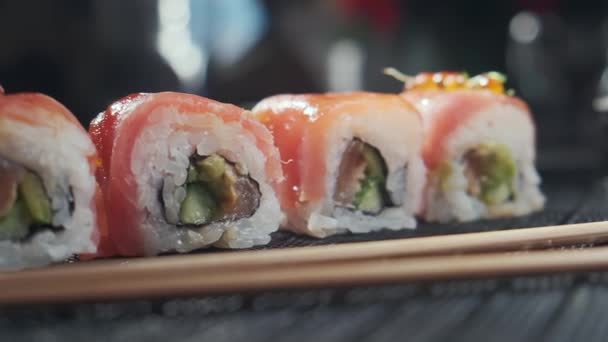 Tiro de close-up deslizante de saborosos rolos de sushi cheios de salmão cru de abacate, atum. Variedade de tipos sushi com peixe, legumes e arroz e pauzinhos Restaurante Sushi, entrega de alimentos. Foco seletivo — Vídeo de Stock