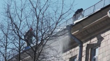 İşçiler şehirdeki çatılardan kar ve buz temizliyor. Kış şehri konsepti