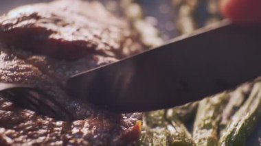 Bifteği çatal ve bıçakla doğramak. Sebzeli ızgara et yemeği. Ağır çekimde kuşkonmaz ile pişirilmiş et parçası.. 