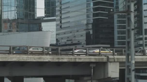 電車の窓から都市の景色。車と道路との橋の建設。背景の高層ビル. — ストック動画