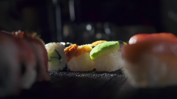 Primer plano de sabrosos rollos de sushi rellenos de salmón crudo de aguacate, anguila. Variedad de tipos de sushi con pescado, verduras y arroz. Restaurante de sushi, reparto de comida. Enfoque selectivo — Vídeos de Stock