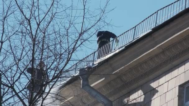 Trabajadores que limpian y tiran nieve y hielo de los techos de la ciudad. Concepto ciudad invierno — Vídeos de Stock