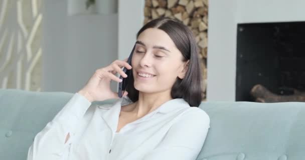 Jovem empresária feminina em acidentes sentados no sofá e falando sobre smartphone em casa. — Vídeo de Stock
