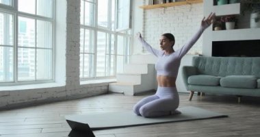 Genç mutlu kadın yoga yapıyor ve nefes egzersizleri yapıyor. Tablet üzerinde canlı video öğrenme dersleri izliyor..