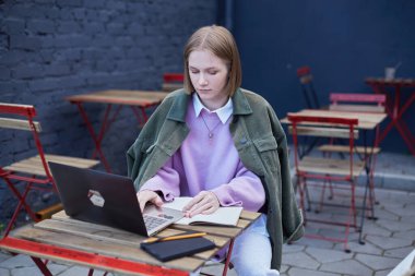 Serbest çalışan genç bir kadın dizüstü bilgisayarının terasında oturuyor.