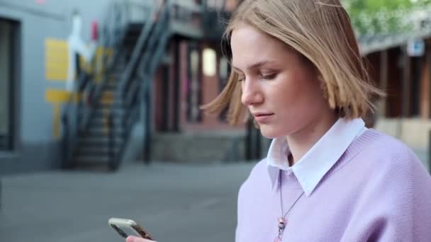 Блондинка с короткими волосами на черном телефоне на улице — стоковое видео