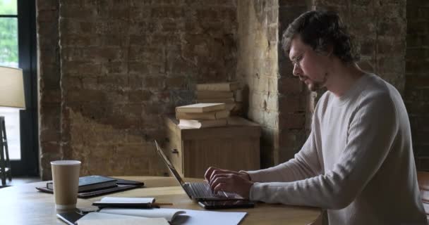 Inteligente jovem freelancer masculino em óculos aprendendo distantemente sentado à mesa com livros e papéis. — Vídeo de Stock