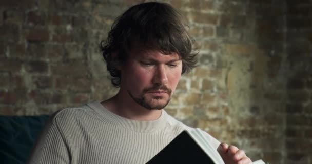 Un jeune homme barbu lit attentivement un livre intéressant — Video