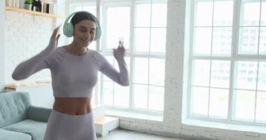 Büyük kulaklıklı genç trend kadın evde müzik dinliyor ve dans ediyor..
