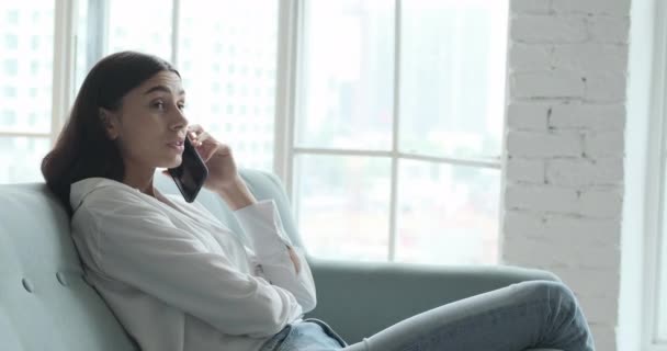 Молодая женщина отдыхает на удобном диване, наслаждаясь прослушиванием лаундж-музыки в прямом эфире через приложение смартфона — стоковое видео