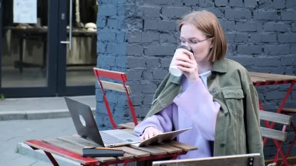 Omtänksam ung affärskvinna skriva på laptop utanför i street cafe — Stockvideo