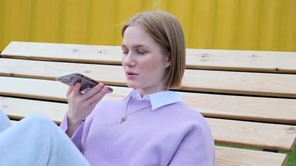 Ung kvinna blond registrerar röstmeddelande på smartphone — Stockvideo