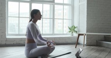 Meditasyon yapan genç bir kadın, nefes almak ve meditasyon yapmak için tablet mobil uygulama kullanıyor.
