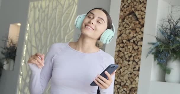 Mutlu, genç bir kadın evde tek başına dans ediyor ve müzik dinlemek için akıllı telefon kullanıyor. — Stok video