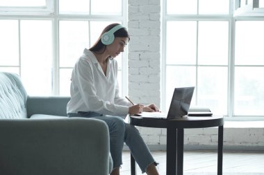 Not defterine yazan ve özel ders ile dizüstü bilgisayara bakan genç bir kadın..