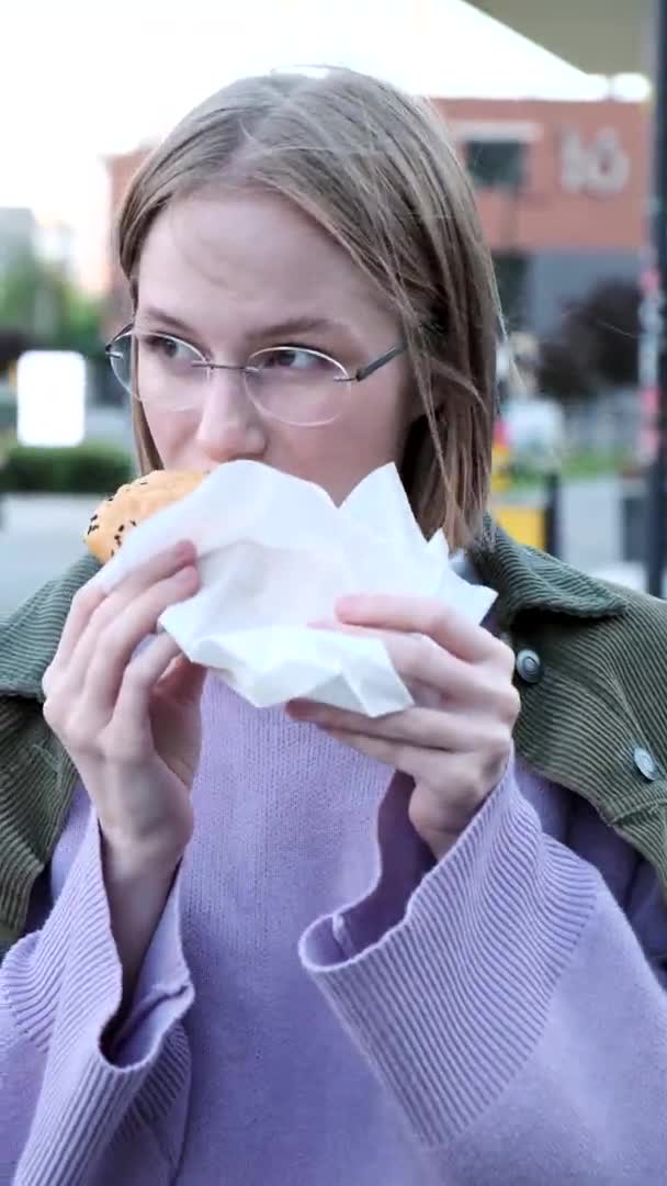 Radostná mladá žena s krátkými vlasy jí burger v kavárně — Stock video