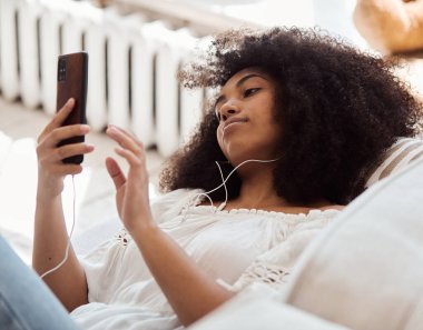 Kablosuz kulaklık kullanan, rahat bir kanepede uzanan sakin, genç bir siyahi bayan.,