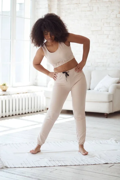 Atletische jonge zwarte vrouw doet de warming-up voor de workout mat thuis met grote ramen in de ochtend. — Stockfoto