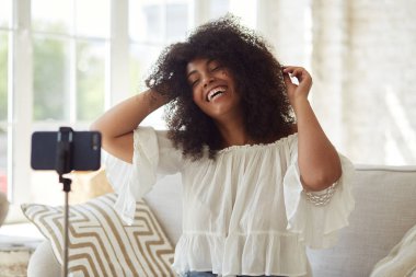 Kadın siyah vlogger etkileyicisi evde oturup kameraya bakıyor.,
