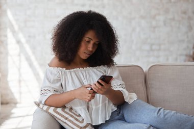 Düşünceli, genç, melez, serbest esmer kadın akıllı telefon koltuğu kullanıyor..