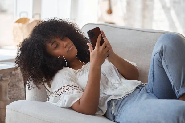 Mujer negra estudiante sentada en el sofá y haciendo videollamada. —  Fotos de Stock