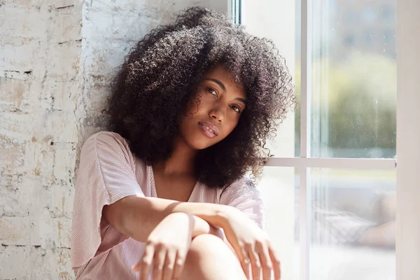 Relajante sonriente joven afroamericana mujer está sentado cerca de la ventana —  Fotos de Stock