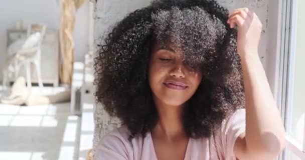 Pihentető mosolygós fiatal fekete nő ül nő ül az ablak mellett — Stock videók
