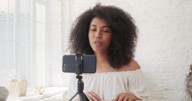 Genç melez kadın akıllı telefondan video kaydı yapıyor. Evde oturuyor..