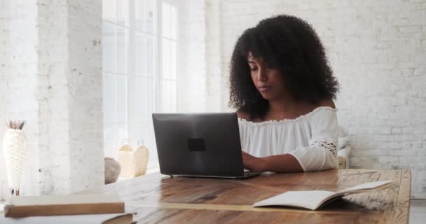 Nachdenkliche junge schwarze Frau tippt auf Laptop am Tisch. — Stockvideo