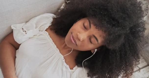 Młoda czarna dama relaksuje się na wygodnej sofie, słuchając na żywo elektroniki otoczenia — Wideo stockowe
