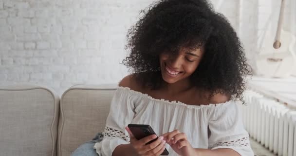 Uma jovem mulher negra africana feliz passando tempo em casa usando seu telefone celular — Vídeo de Stock