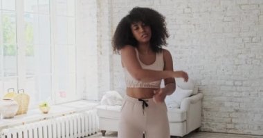 Genç melez kadın kollarını ve bacaklarını uzatıyor ve sabahları büyük pencereler açıyor..