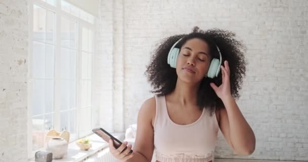 Молода модна жінка у великих навушниках слухає музику і танцює вдома . — стокове відео