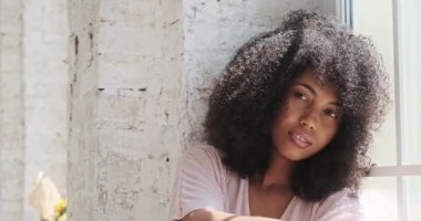 Rahatlatıcı gülümseyen Afro-Amerikan kadın pencerenin yanında oturuyor.