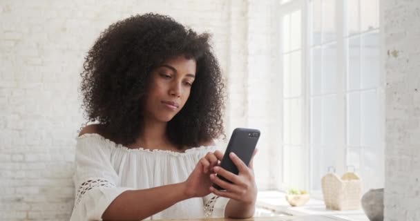 En lycklig ung svart afrikansk kvinna spenderar tid hemma med sin mobiltelefon — Stockvideo