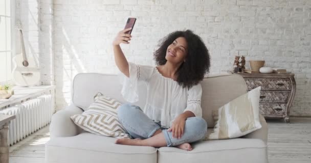 Junge Frau mit gemischter Rasse schaut auf Smartphone-Bildschirm, macht Selfies, schwarze trendige Frau genießt Online — Stockvideo