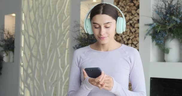 Happy ceria wanita muda menari sendirian di rumah dan menggunakan smartphone untuk mendengarkan musik — Stok Video