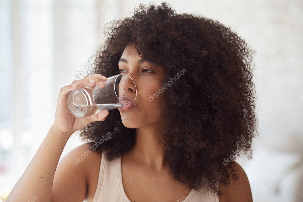 Young multiracial woman drinking water daily morning habit routine after morning exercise