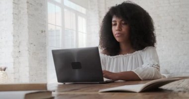Laptop kullanarak sınavlara hazırlanan ve masada oturan odaklanmış siyahi bir kız öğrenci..