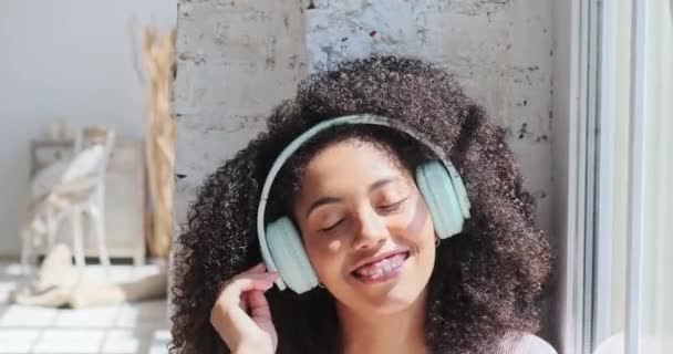 Gelukkig grappig zwart multiraciale dame dragen van koptelefoon in de buurt van het raam — Stockvideo