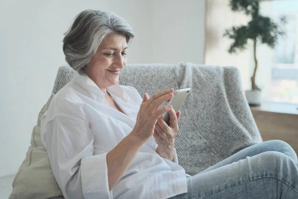 Happy older middle aged female using smartphone, enjoying chat with children