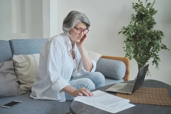 Una anciana usa un portátil, calculando sus ahorros y frustrándose con deudas y facturas enormes. — Foto de Stock