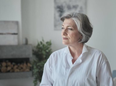 Kendinden emin, eğitimli yaşlı bir bayan yönetici parlak çağdaş bir iş yerinde duruyor ve ciddi görünüyor.