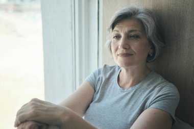 Yaşlı, düşünceli, özürlü yaşlı bir kadın hastaneden dışarı bakıyor ve gülümsüyor.