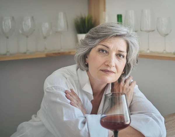 Elderly Caucasian woman enjoys a glass of red wine and remembering pleasant moments