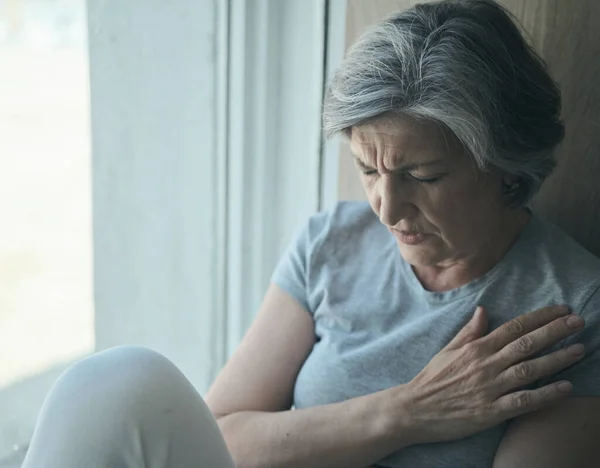 Oudere oudere zieke gehandicapte, verdrietige vrouw in pijn en lijden zittend bij het raam in het ziekenhuis. — Stockfoto